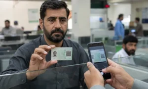 Pakistani citizen holds a new QR code-based identity card while it is scanned with a smartphone at a government service counter.